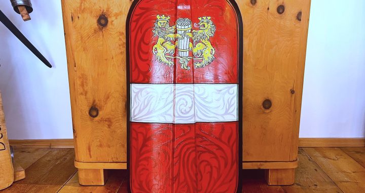 Handbemalte Pavese mit Haller Stadtwappen – zwei goldene Löwen mit Salzfass, Ei-Tempera auf Kreidegrund, gefertigt von Wappenwerk. Im Hintergrund ein Holzschrank.